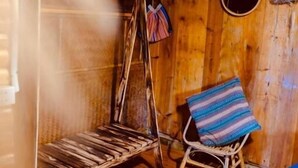 Tunnelmallinen, maalaishenkinen huone, jossa on puulattia, keinutuoli, pyöreä ikkuna ja kuviollinen koristetyyny.