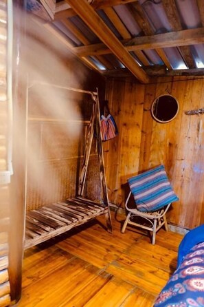 Une pièce rustique en bois, avec une balançoire, une fenêtre ronde et un coussin à motifs.