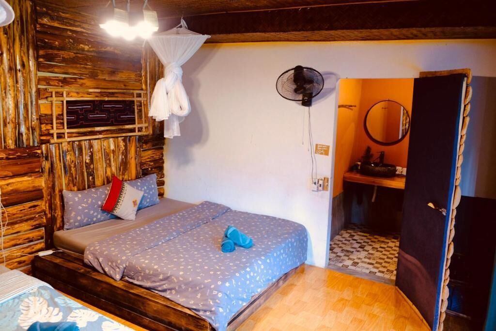 Una habitación con cama, ventilador, espejo y una puerta que da a otra habitación.