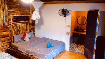 Una habitación con cama, ventilador, espejo y una puerta que da a otra habitación.