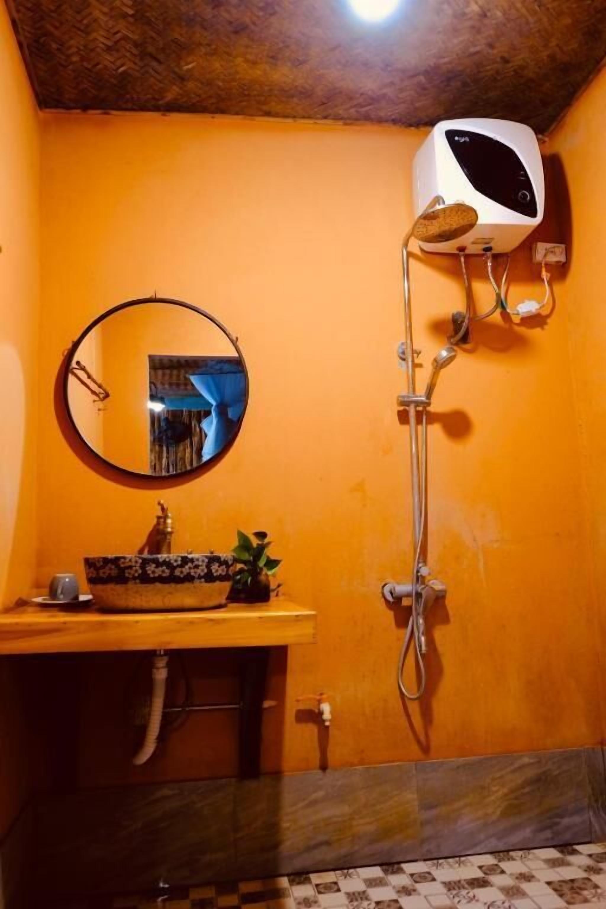 A bathroom with a wooden vanity, a round mirror, a sink, and a shower with a handheld showerhead.