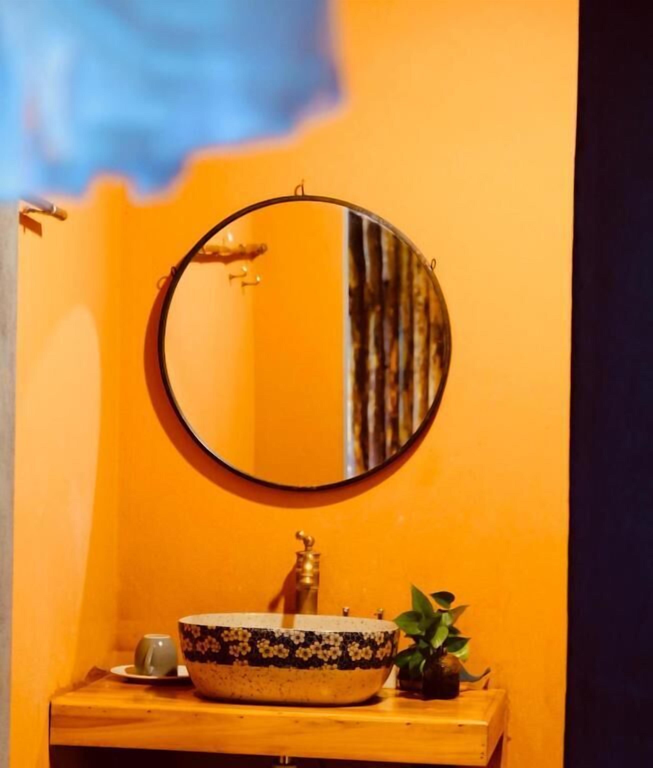 A bathroom with a round mirror, a sink with a decorative bowl, a small plant, and a cup on the counter.