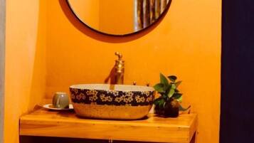 A bathroom with a round mirror, a sink with a decorative bowl, a small plant, and a cup on the counter.
