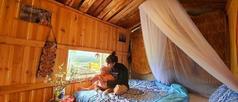 Una habitación con piso de madera, una cama, un ventanal y un adorno colgante.