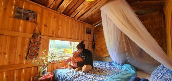 A wooden room with a bed, a window, and a hanging decorative item.