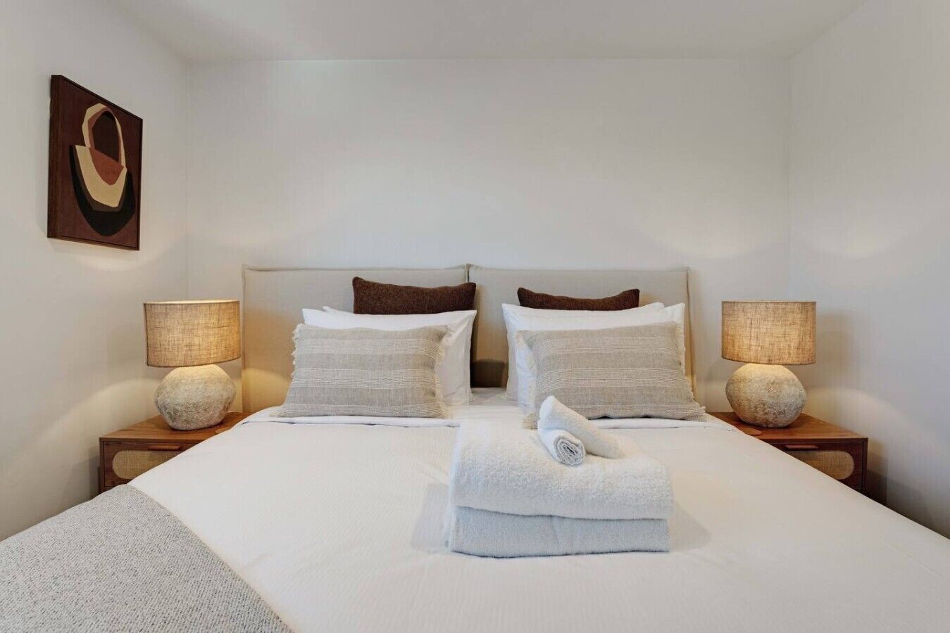 A hotel room with a large bed, two bedside tables, two lamps, and a painting on the wall.