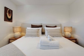 A hotel room with a large bed, two bedside tables, two lamps, and a painting on the wall.
