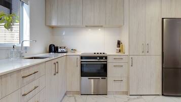 A modern kitchen with light wood cabinets, stainless steel appliances, and a marble floor.