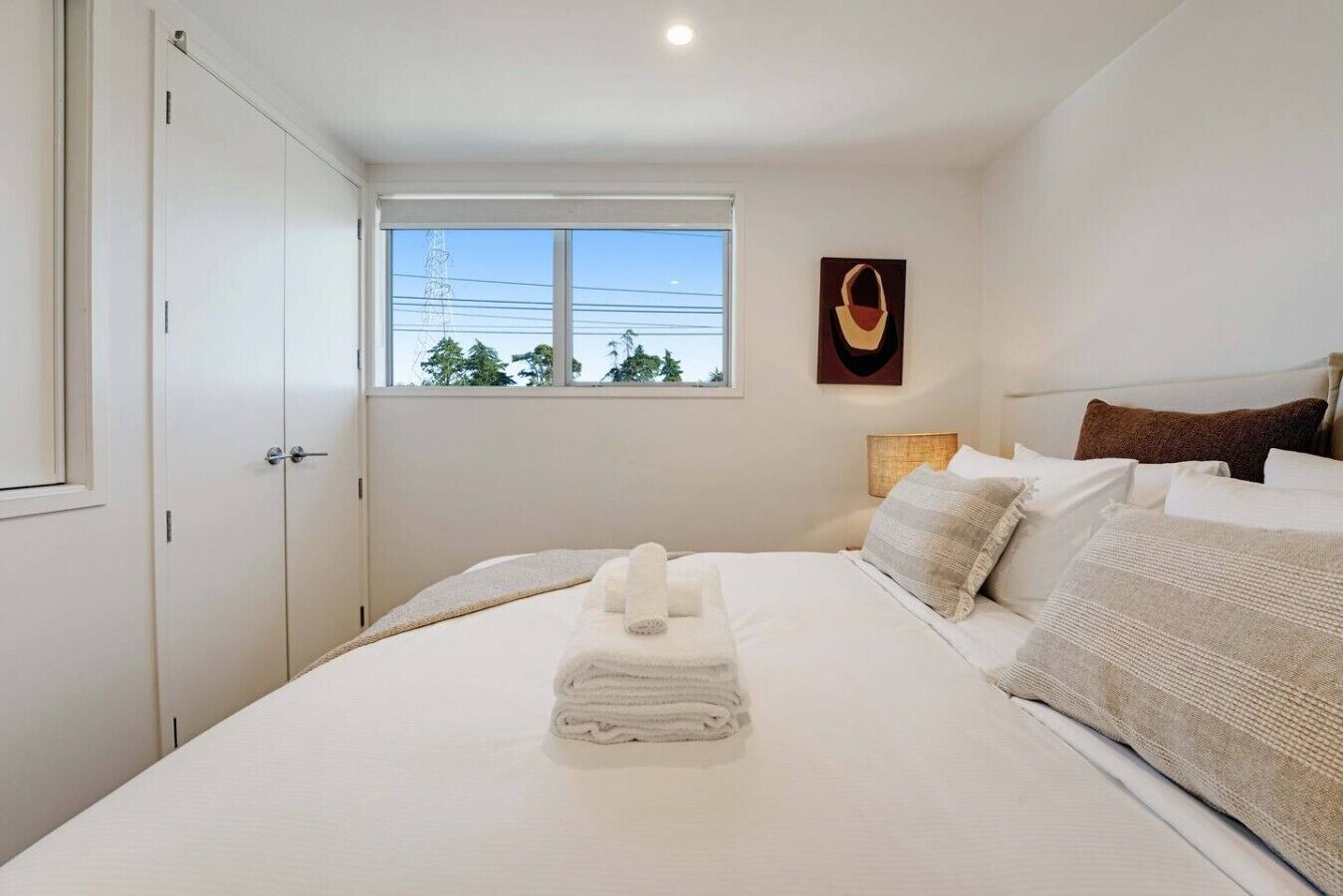 Ein Schlafzimmer mit Bett, Fenster, Wandbild und Tür.
