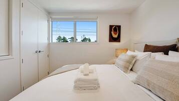 Ein Schlafzimmer mit Bett, Fenster, Wandbild und Tür.
