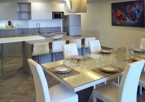 Une cuisine moderne avec un îlot central, une table à manger pour six personnes et un tableau accroché au mur.