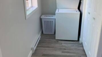 A laundry room with a washer and dryer, a laundry basket, and a sign on the wall.