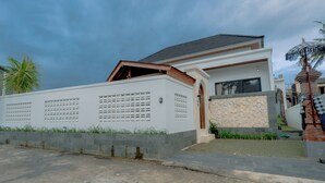 Una casa moderna con fachada blanca, un muro de piedra y una puerta de metal.
