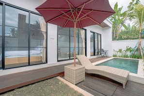 Un área de piscina moderna al aire libre con una silla de descanso y una sombrilla, amplias ventanas y vistas del paisaje circundante.