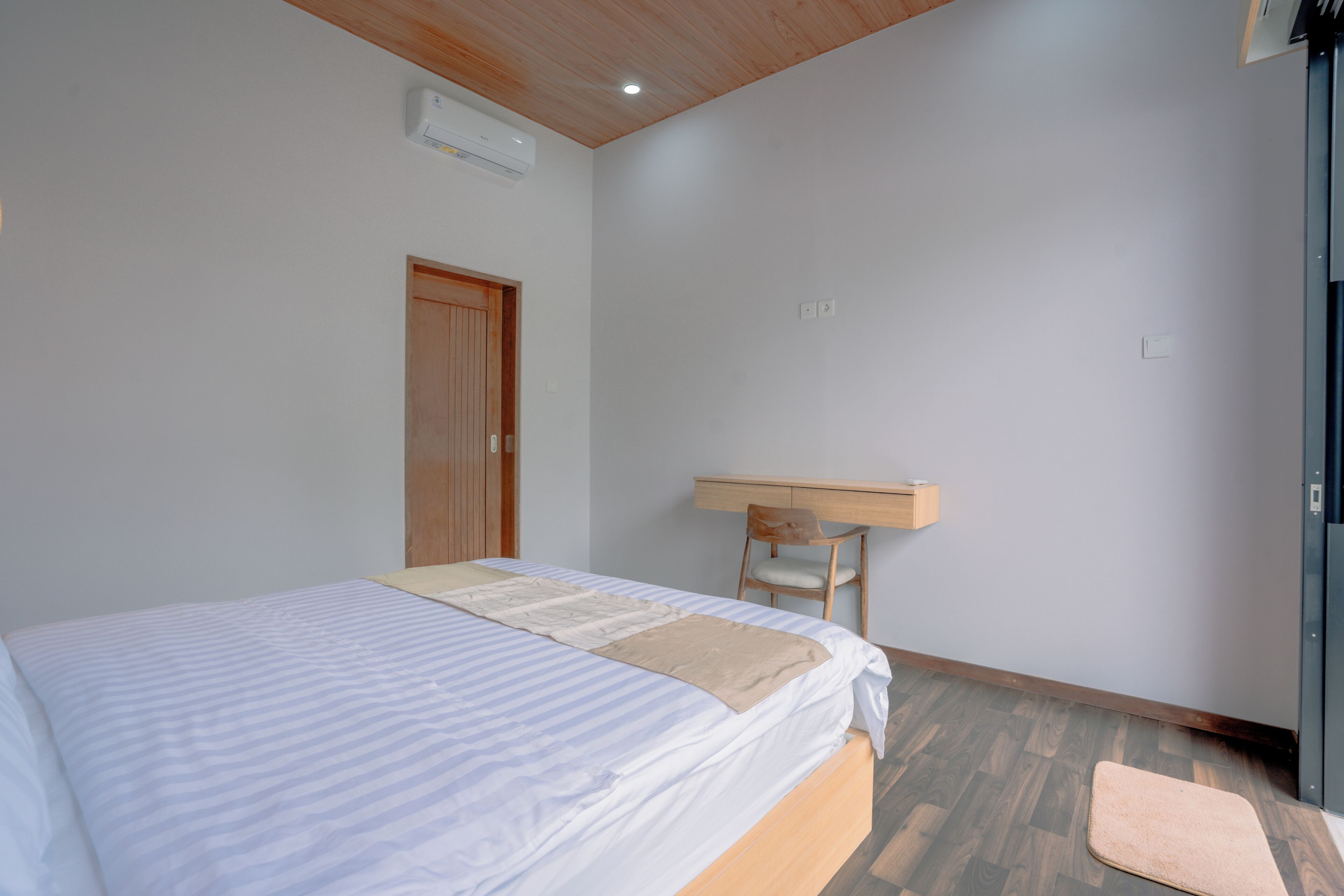 Un dormitorio con cama, un escritorio de madera, una silla y piso de madera.