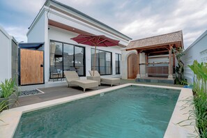 Una casa moderna con piscina, mobiliario exterior y un patio cubierto.