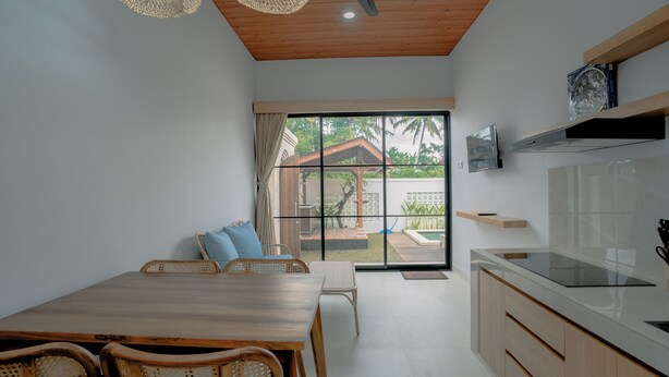 Una cocina moderna con comedor, techo de madera y grandes puertas correderas de vidrio que dan a un espacio exterior.