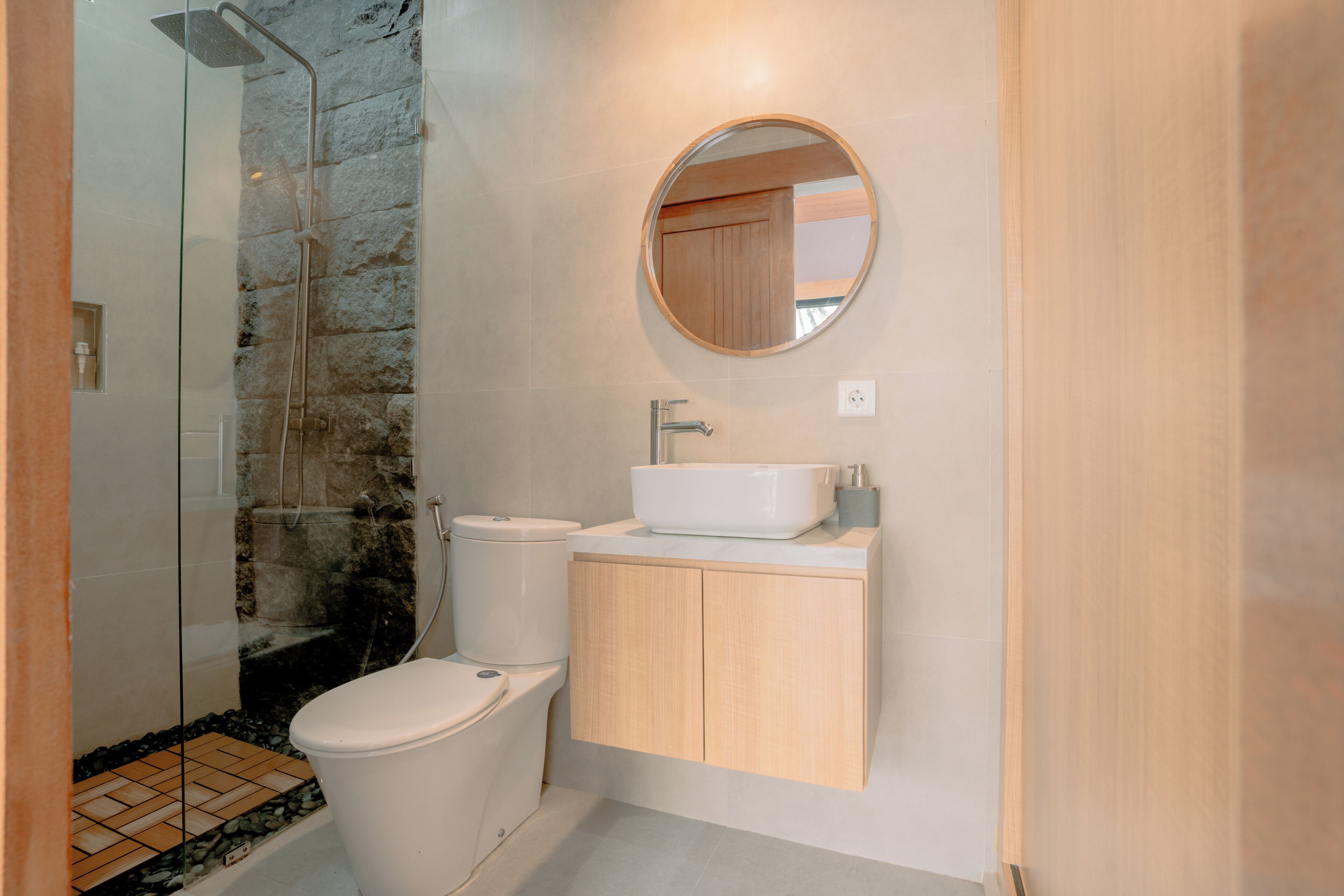 A modern bathroom with a glass shower enclosure, a toilet, a sink, and a wooden vanity.