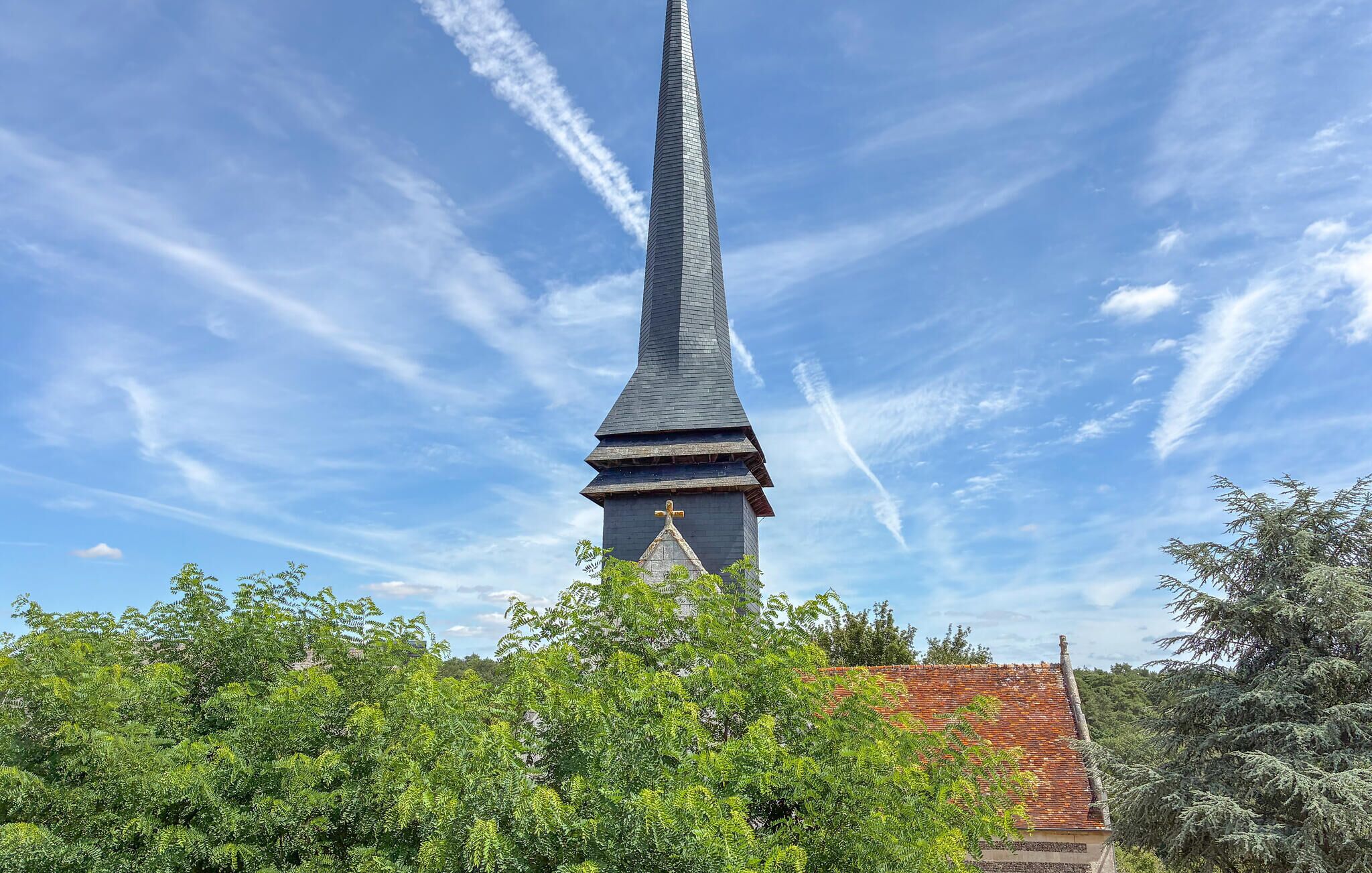 Een kerktoren met een kruis bovenop, omringd door groen.