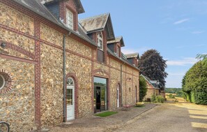 Ein Steinhaus mit mehreren Fenstern und Türen, einer Schotterauffahrt und einem von Bäumen gesäumten Hintergrund.