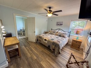 Ein Schlafzimmer mit einem Bett, einem Deckenventilator, einem Nachttisch, einem Schreibtisch mit Stuhl und einem Fenster mit Jalousien.