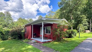 Ein rotes Einfamilienhaus mit überdachter Veranda, umgeben von üppigem Grün und Bäumen.