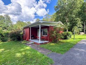 Ein rotes Einfamilienhaus mit überdachter Veranda, umgeben von üppigem Grün und Bäumen.