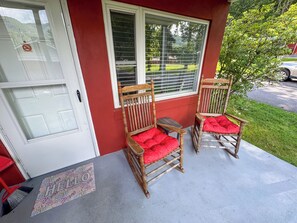 Eine Veranda mit zwei hölzernen Schaukelstühlen mit roten Kissen, einem kleinen Tisch und einer Tür mit einem 'No Parking'-Schild.