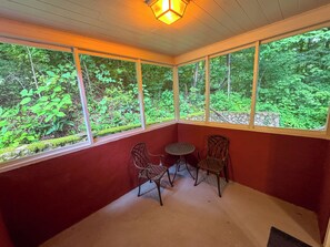 Une pièce avec un mur rouge, un ventilateur de plafond et une vue sur une forêt, visible à travers de grandes fenêtres.