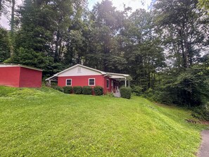 A red house with a porch, surrounded by lush green grass and trees. - The Honey Bear Retreat nestled in the heart of Maggie Valley (Maggie Valley)