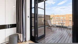 En balkong med utsikt över en byggnad med tegelstensfasad, en stol och ett litet bord.
