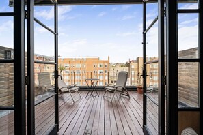 Ein Balkon mit Holzboden, zwei Stühlen, einem kleinen Tisch und einem Blumentopf.