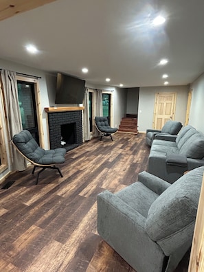 A living room with a fireplace, two armchairs, a sofa, and a wooden floor.