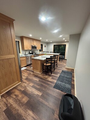 A modern kitchen with wooden cabinets, a central island, and a dining area with chairs.
