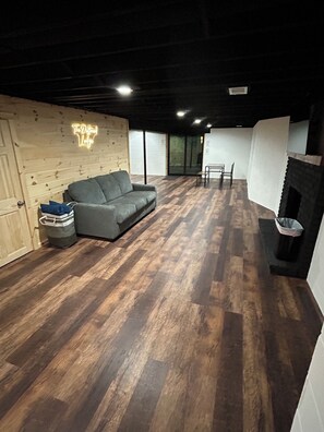 A room with a wooden floor, a grey sofa, a small table, and a fireplace.