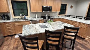 A modern kitchen with wooden cabinets, a marble countertop, and a central island with chairs.