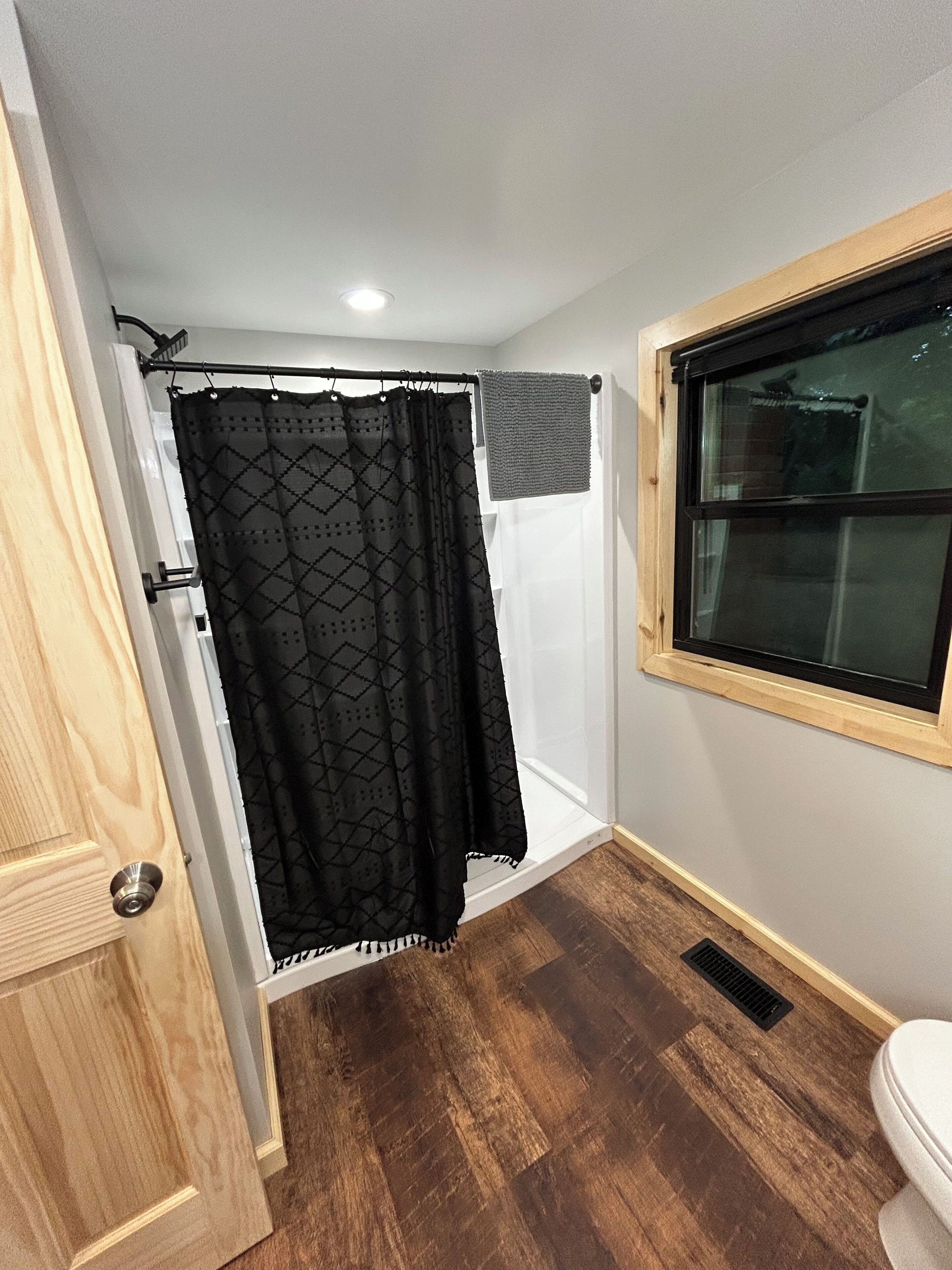 A bathroom with a shower, a toilet, and a window.