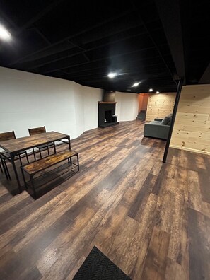 A room with a wooden floor, a dining table with chairs, a sofa, and a fireplace.