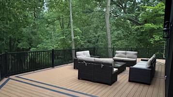 A deck with outdoor furniture, surrounded by a black railing and trees.