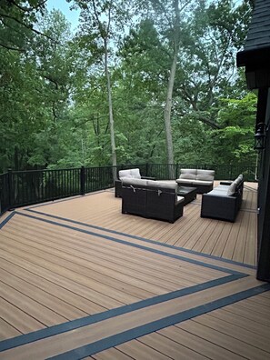 A deck with outdoor furniture, surrounded by a black railing and trees.