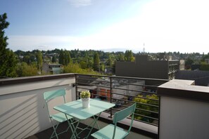Ein Balkon mit Tisch und Stühlen, einem Blumentopf und einer Stadtansicht im Hintergrund.