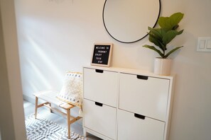 A room with a white cabinet, a small table with a patterned cushion, a sign on the wall, and a potted plant. - Timeless 3BR Retreat Central Fremont (Seattle)
