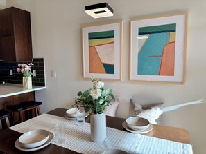A dining area with a table set for two, a vase with flowers, and two framed abstract paintings on the wall. - Timeless 3BR Retreat Central Fremont (Seattle)