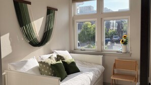 Um quarto com cama, janela com vista, planta pendurada e uma cadeira.