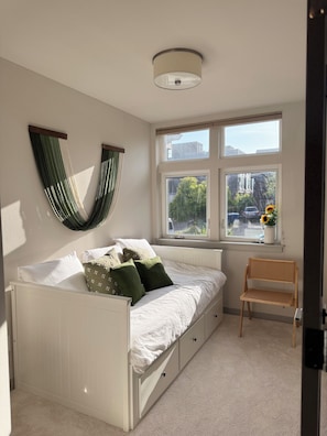 A bedroom with a bed, a window with a view, a hanging plant, and a chair. - Timeless 3BR Retreat Central Fremont (Seattle)