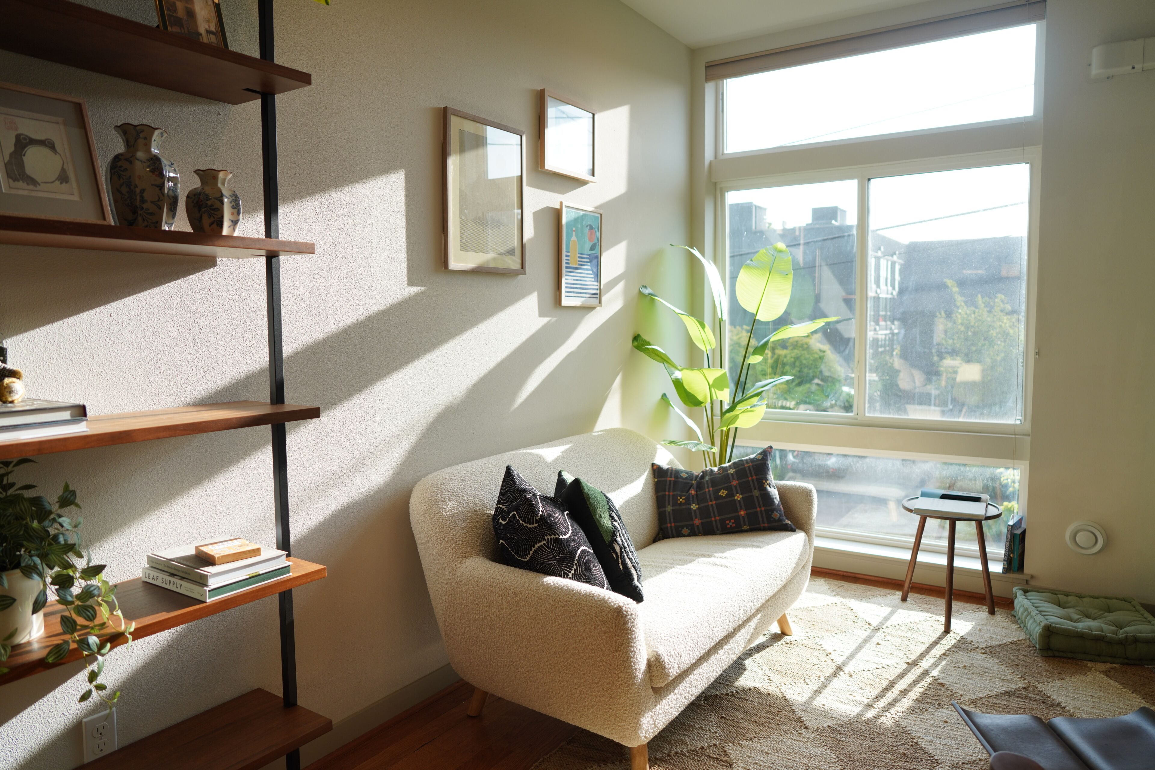 Un salon confortable avec un canapé, une petite table d’appoint et une grande fenêtre donnant sur des immeubles.