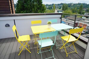 A balcony with a yellow and green table and chairs, a potted plant, and a view of the city. - Timeless 3BR Retreat Central Fremont (Seattle)