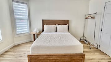 A bedroom with a wooden bed, a bedside table, a hanging light fixture, a wardrobe, and a window with blinds.