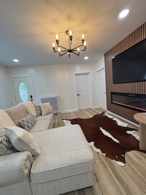 Una sala de estar moderna con un sofá seccional, una chimenea, un televisor montado y un candelabro.
