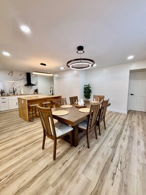 A modern kitchen with a dining area, wooden flooring, and contemporary lighting fixtures.